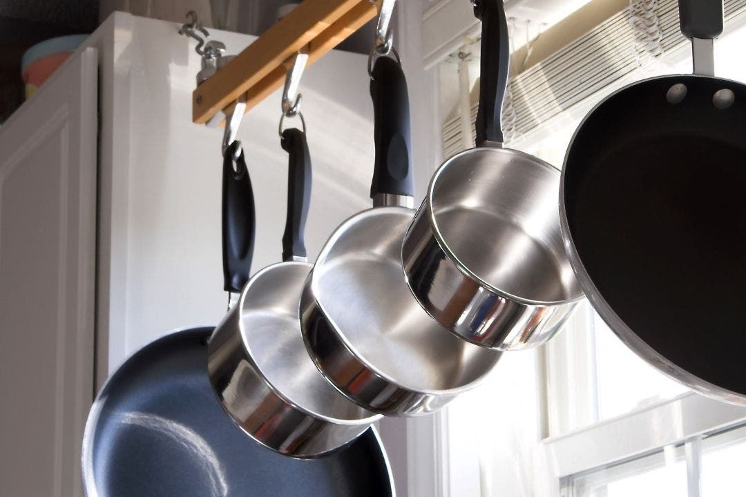 Stainless steel pots and pans hanging on kitchen rack near window