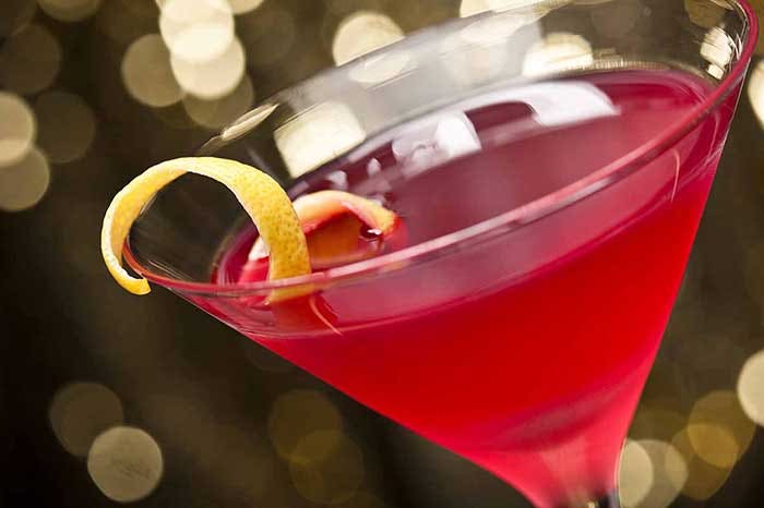 Cosmopolitan cocktail with lemon garnish in front of a gold glitter background