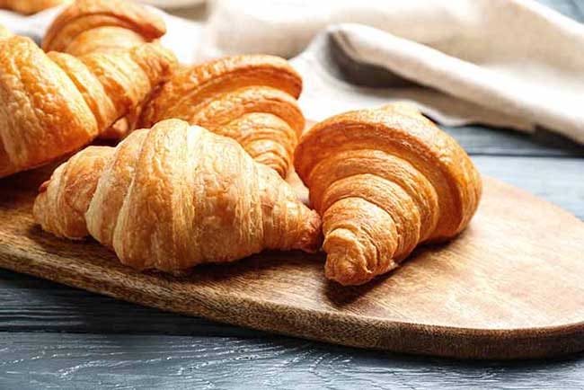Board with tasty croissants on dark wooden table, closeup.