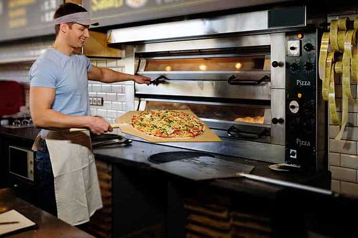 Handsome pizzaiolo making pizza at kitchen in pizzeria.