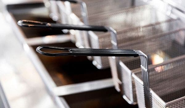 Commercial deep fryer baskets with black handles in a professional kitchen setup.