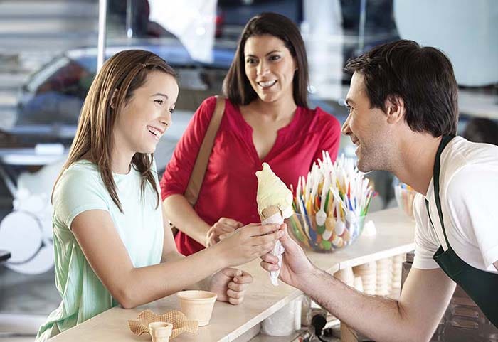 Man handing ice cream to a kid with her mom in the background