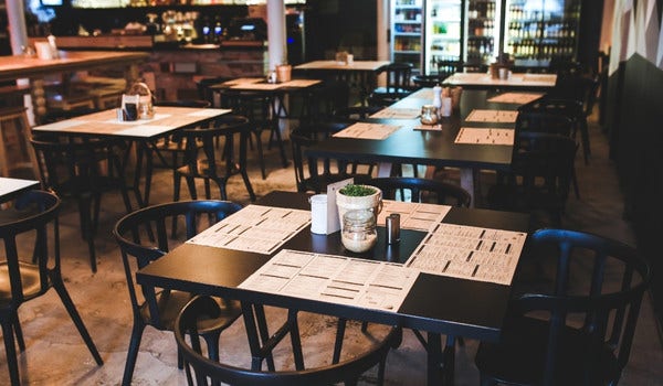 Inside of a resturant dining room with black charis, black tables, menus, and condiments.
