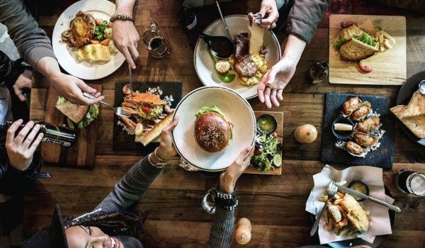 Overhead view of friends sharing a diverse meal with burgers, steak, and seafood on a rustic table.