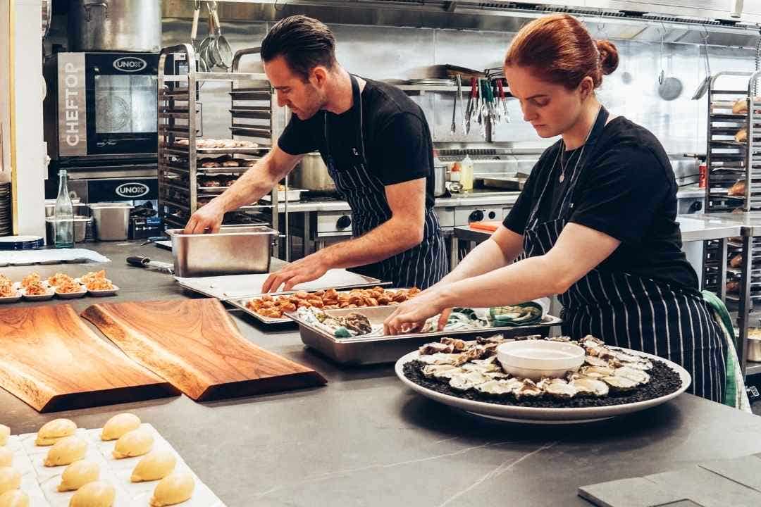 Chefs preparing plated food in a commercial catering kitchen workspace.