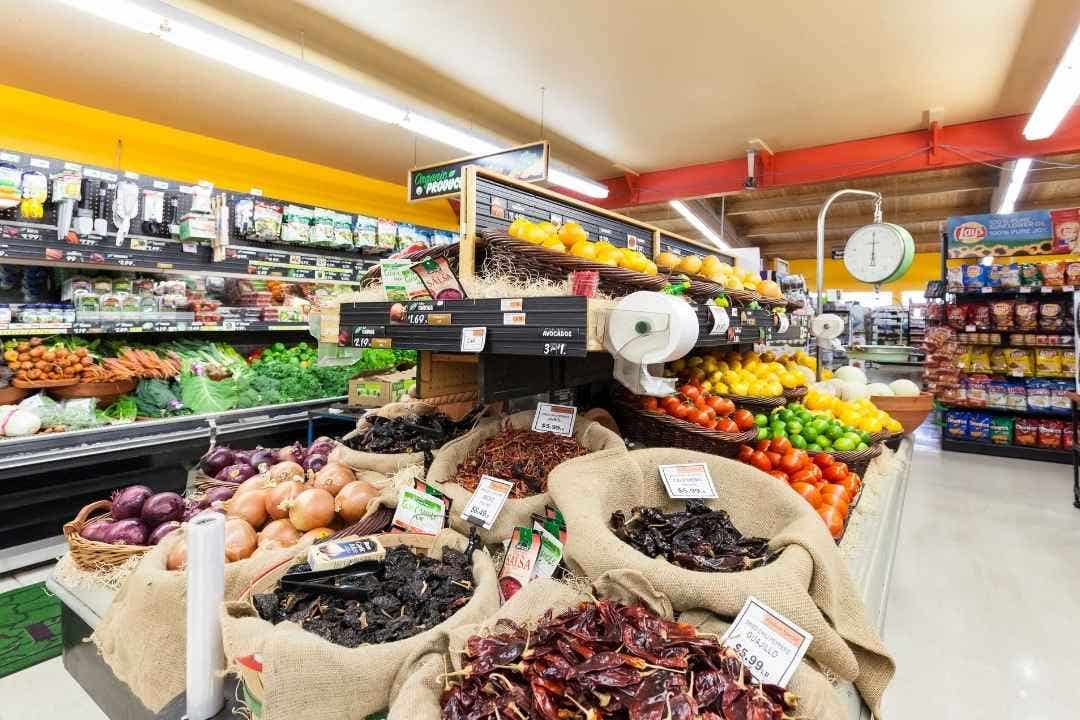 Colorful produce display with onions, peppers, and dried chiles in grocery aisle.