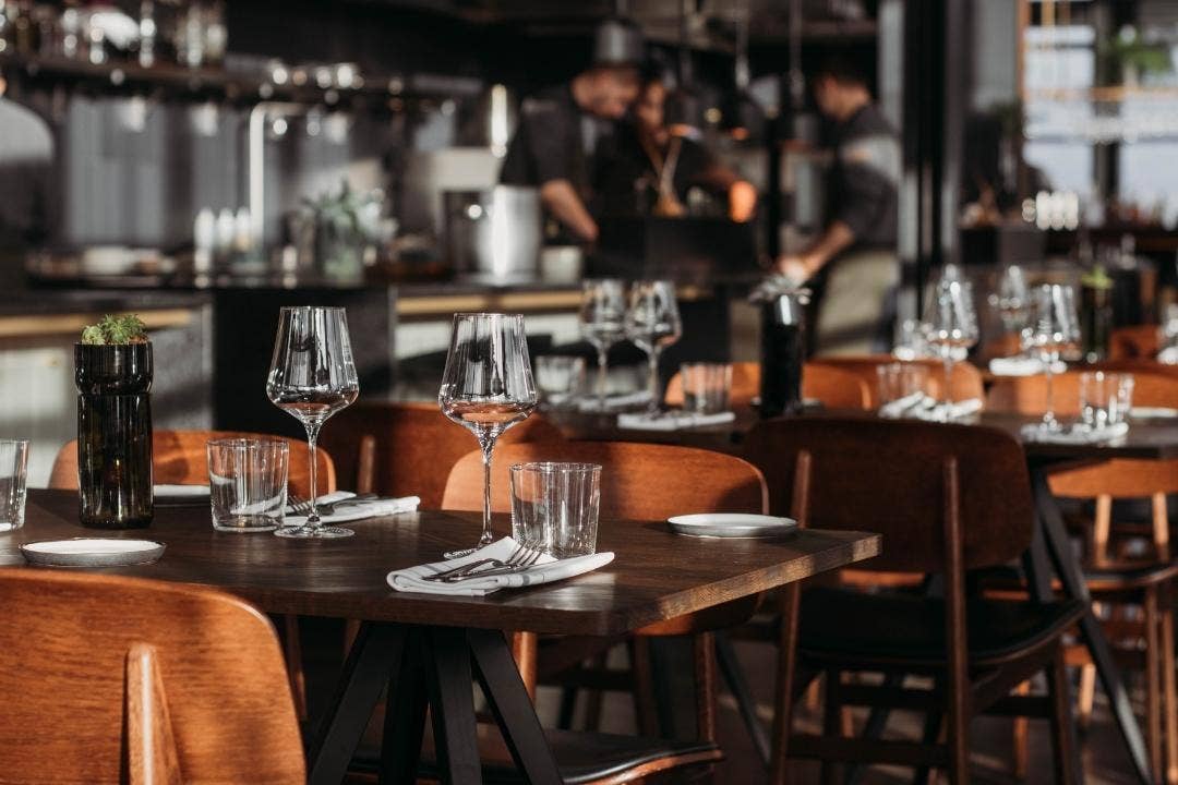 Modern restaurant with set tables and chefs working in an open kitchen.