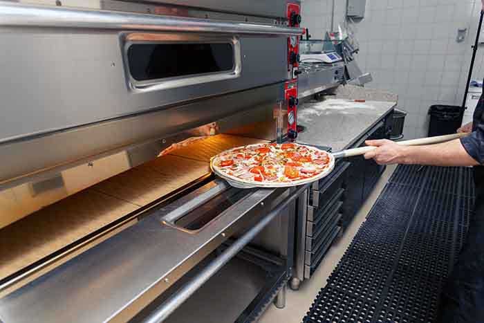 cook putting pizza in electric oven in a pizzeria