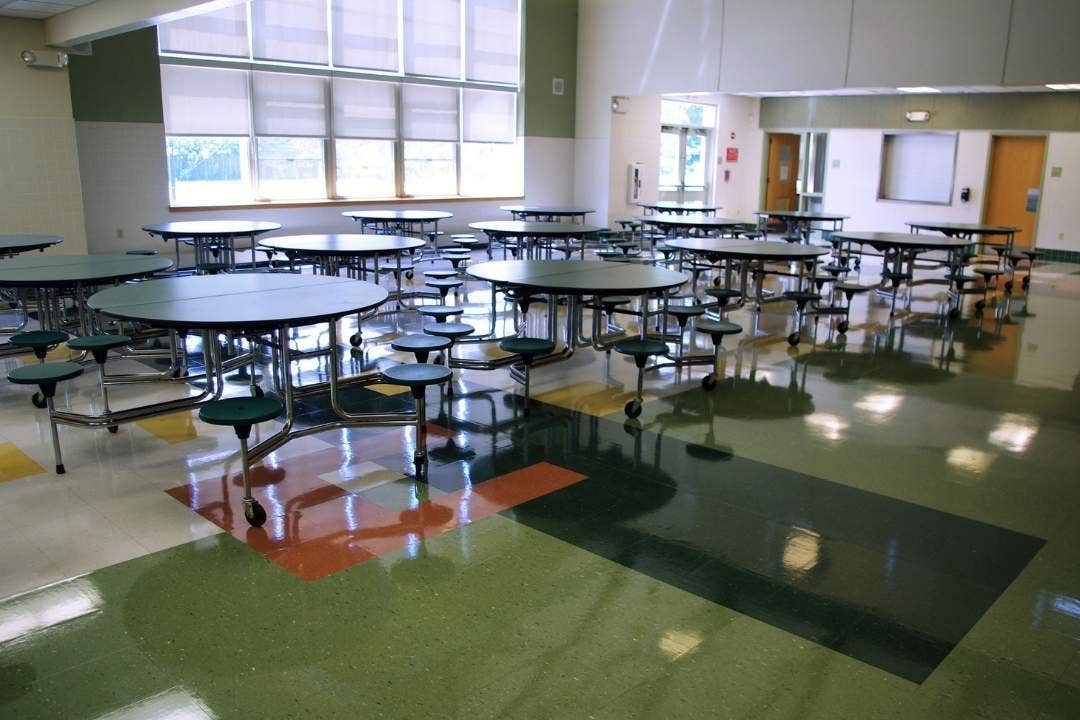Empty cafeteria with round tables and built-in stools on a polished tile floor.