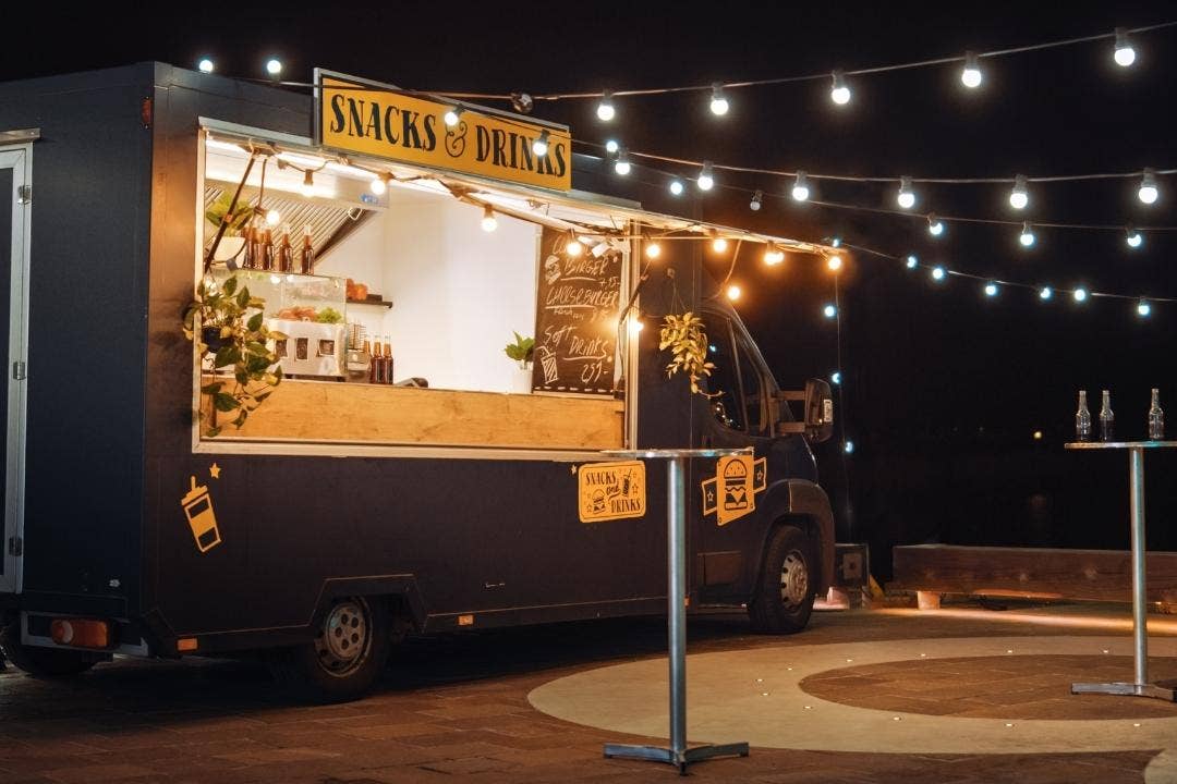Lit food truck serving snacks and drinks under string lights at an outdoor event.