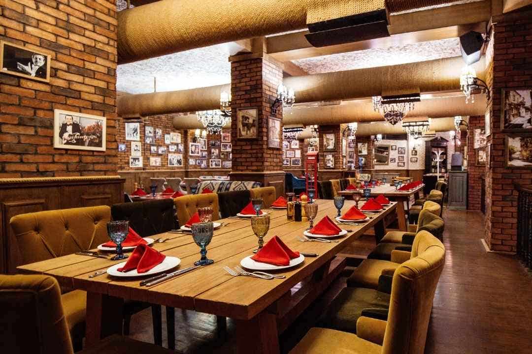 Elegant restaurant with brick walls, chandeliers, and tables set with red napkins.
