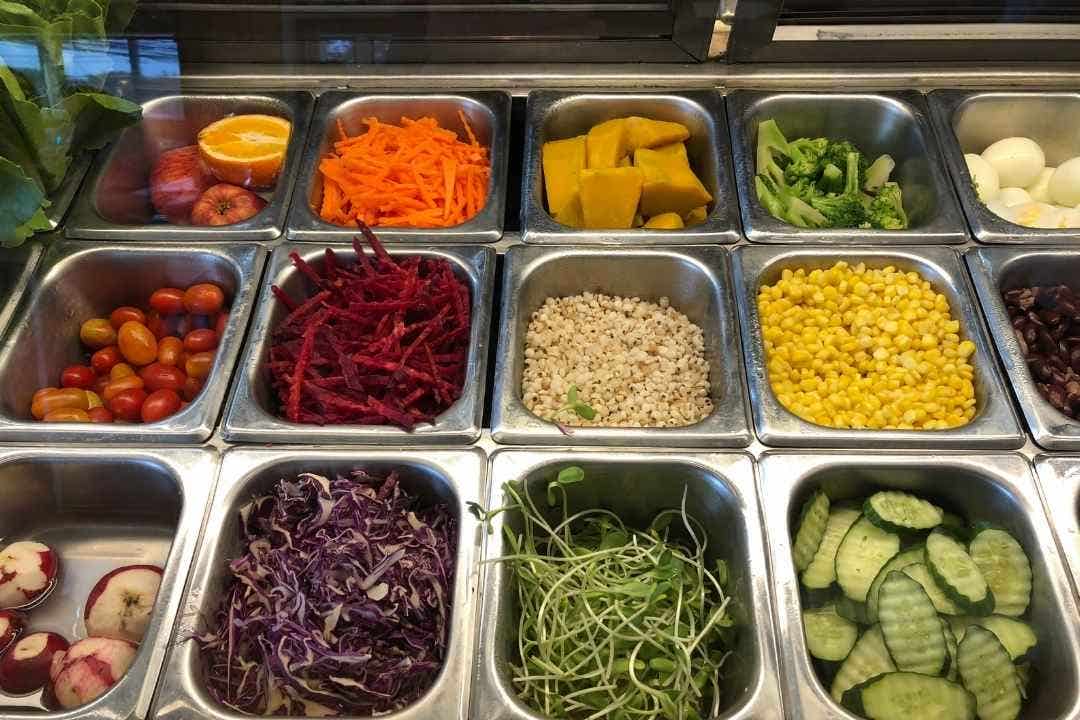 Stainless steel food pans filled with fresh salad bar vegetables and toppings