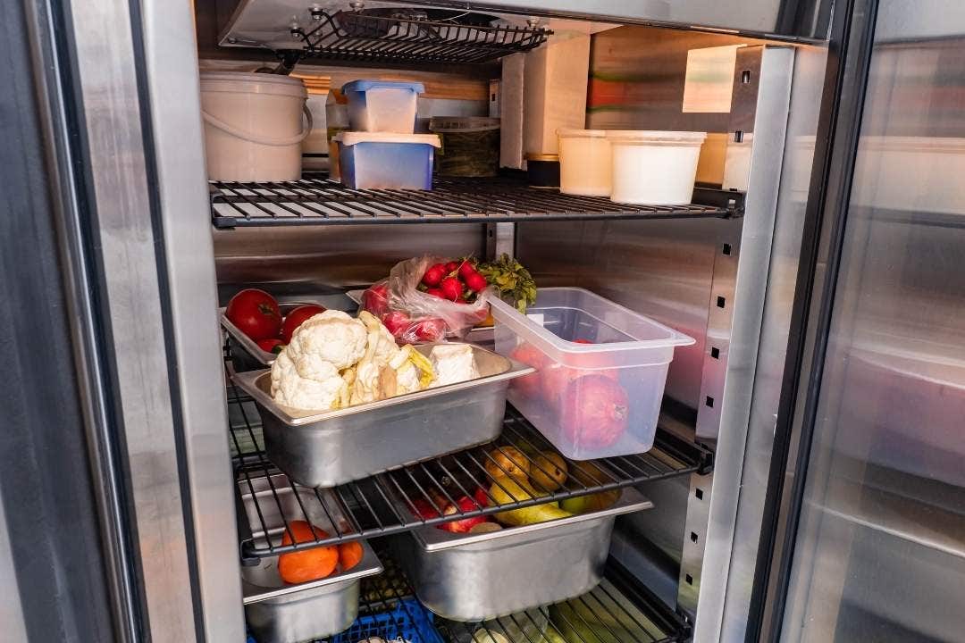Stainless steel food pans storing vegetables inside a commercial refrigerator