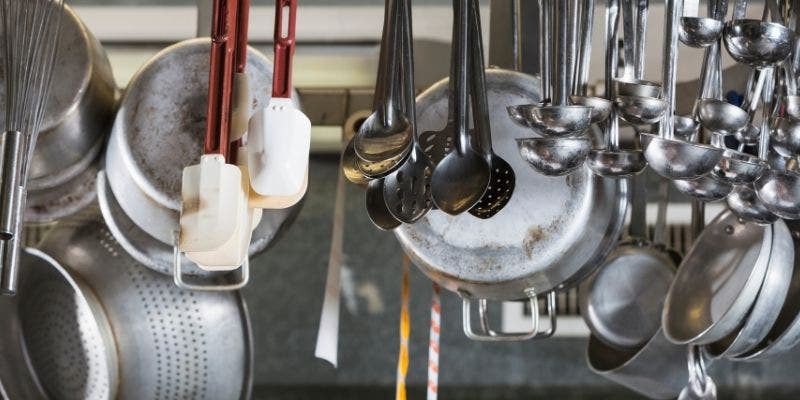 Utensils such as spoons, whisks, spatulas, pots and pans hanging in a commercial kitchen.