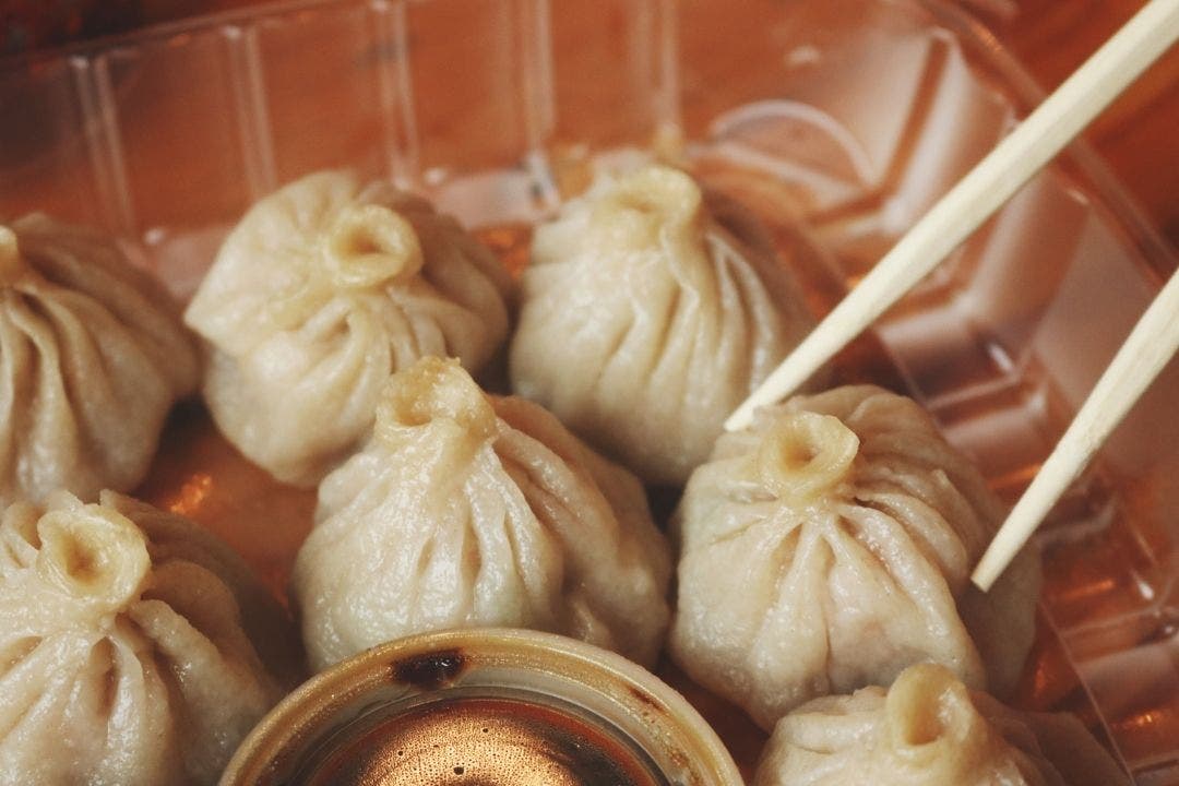 Close-up of steamed dumplings with chopsticks and dipping sauce in takeout tray