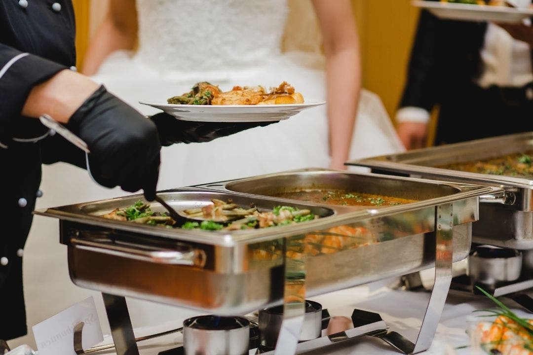 Chef serving hot food from chafing dishes at a wedding buffet catering line