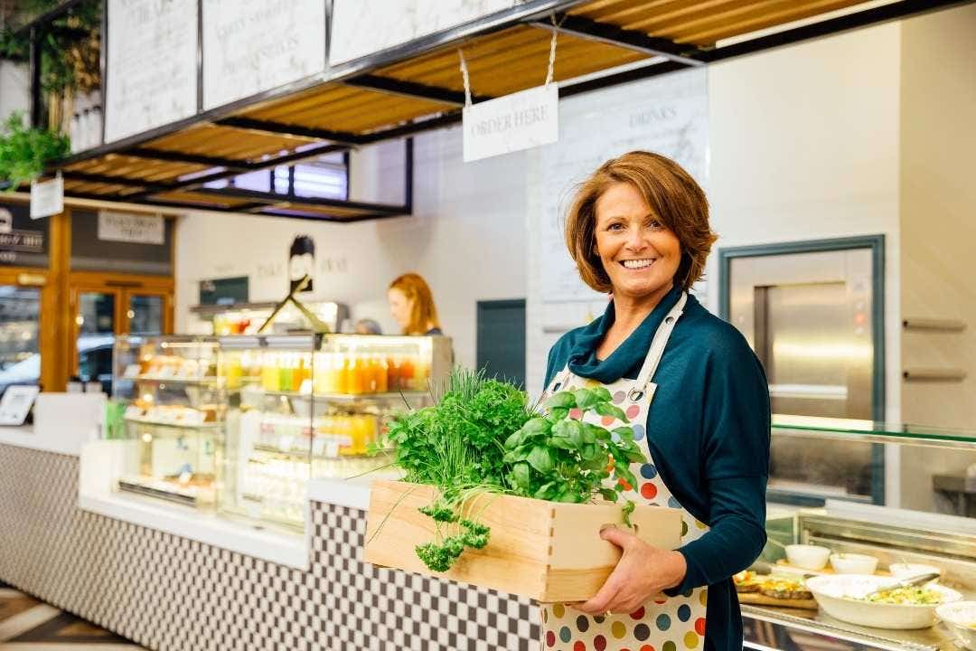 Smiling woman in café holding fresh herbs near healthy food and juice display
