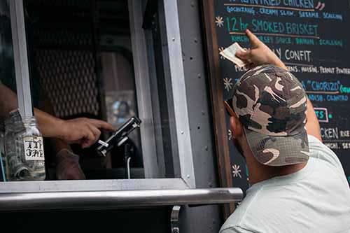 Man points to menu on the side of a food truck while ordering.