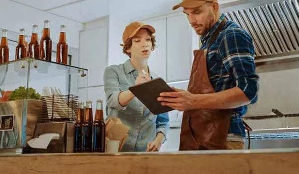 Small business owners discussing orders on a tablet at a food counter.