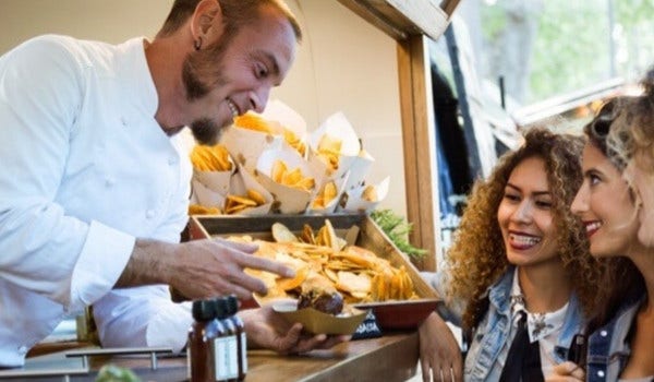 chef handing food to female customers out of a food truck.