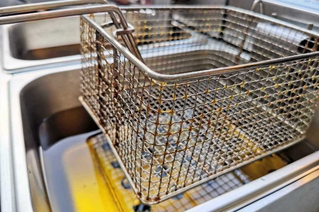 Close-up of commercial deep fryer basket with oil in a stainless steel food truck kitchen setup.