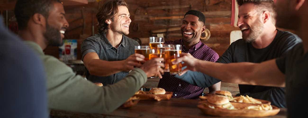 Male Friends Drinking Beer And Eating Burgers In Sports Bar