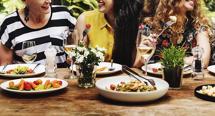 A group of women socialize at a restaurant with plates of food on the table.