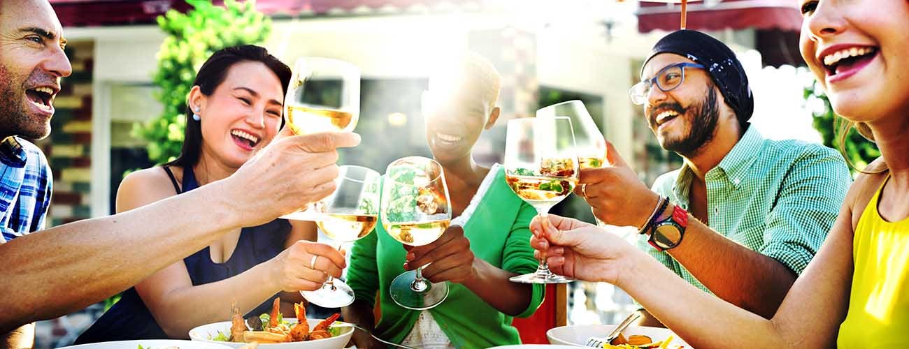 A diverse group of friends celebrating with wine glasses while enjoying dinner at an outdoor restaurant.