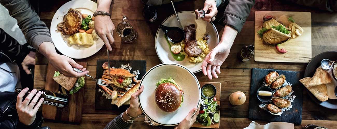 Friends at a restaurant having meal passing plates and sharing food.