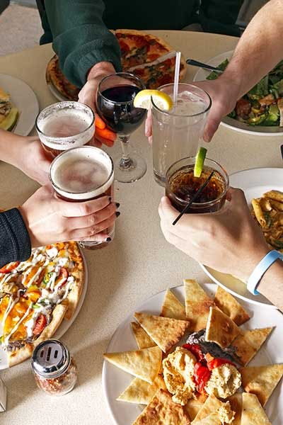 Friends raise their glasses to toast over their table of food at a restaurant.