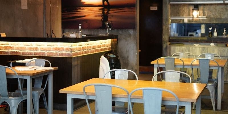 Inside of a casual restaurant dining room with tables and chairs and a checkout counter.