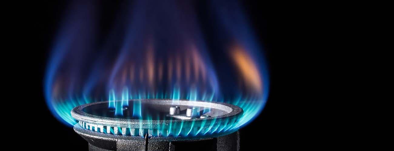 A blue flame comes from a gas burner set against a black background.