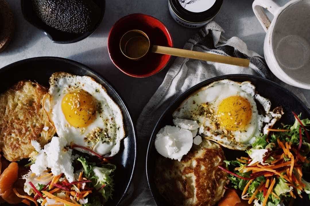 Griddled breakfast plate with eggs, pancakes, salad, and cheese on a dark ceramic dish.