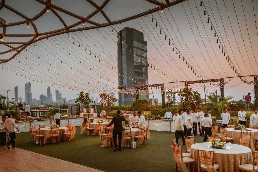 Rooftop catering event at sunset with string lights and city skyline in the background