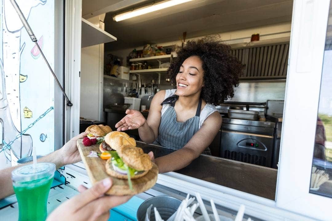 Smiling food truck worker handing out fresh sandwiches from service window