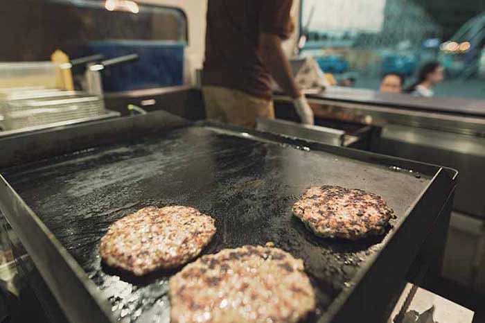 A close up meat patties on the grill for cooking burgers inside the food truck van.