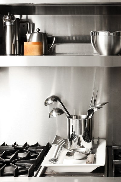 Commercial cooking equipment and smallwares. Stainless steel mixing bowl, ladles, spatula, and spice holders on top of a stainless steel range.
