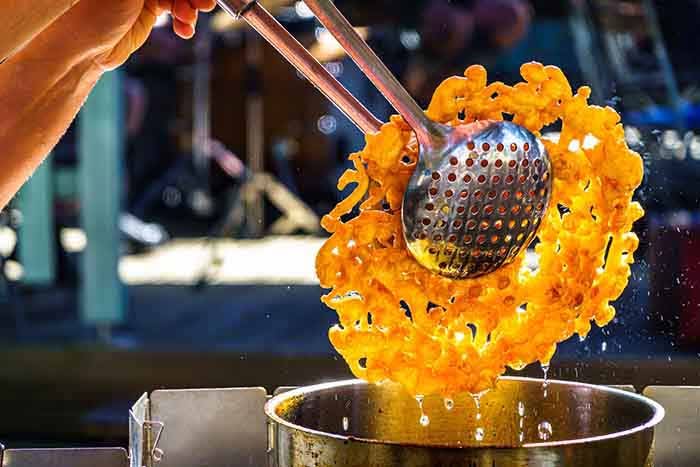 Funnel Cake being pulled out of a deep fryer.