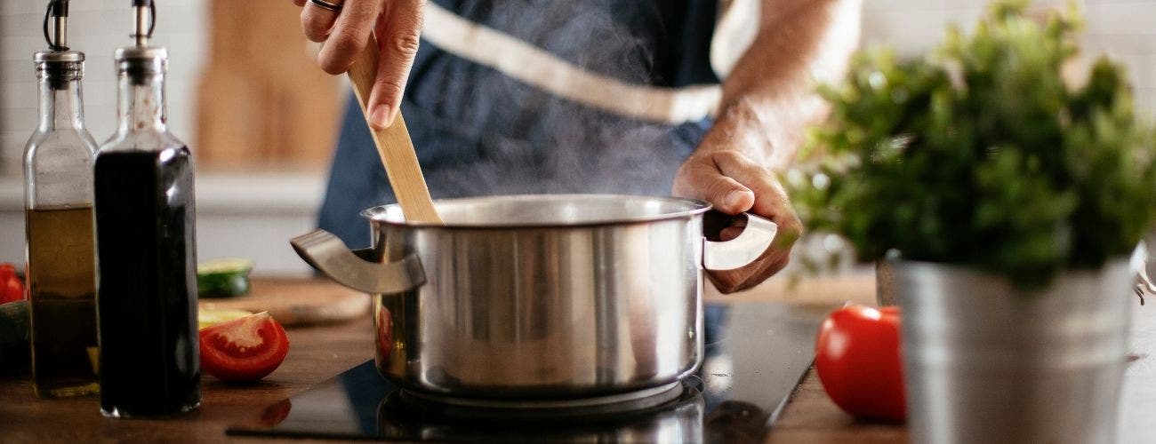 Home chef cooking and stirrin a stainless steel sauce pot with wooden spoon.