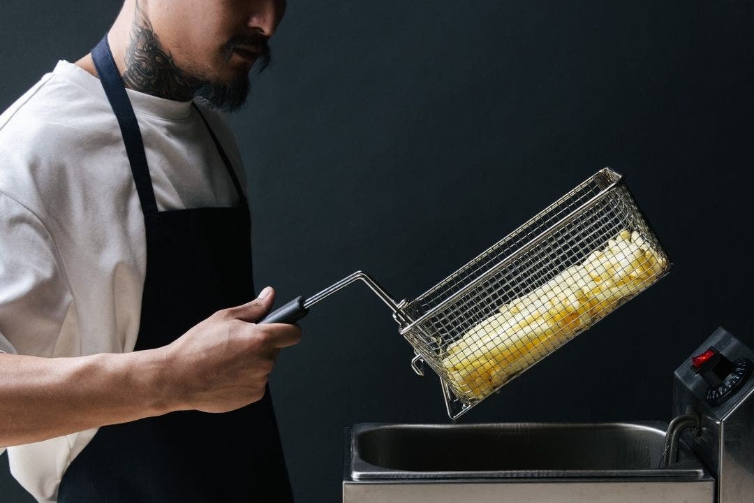 Man frying french fries in deep fryer basket with black background.