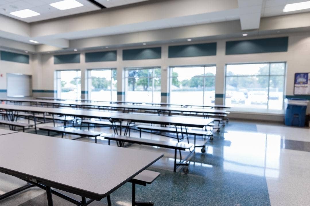 Empty school cafeteria with long tables and large windows during daytime
