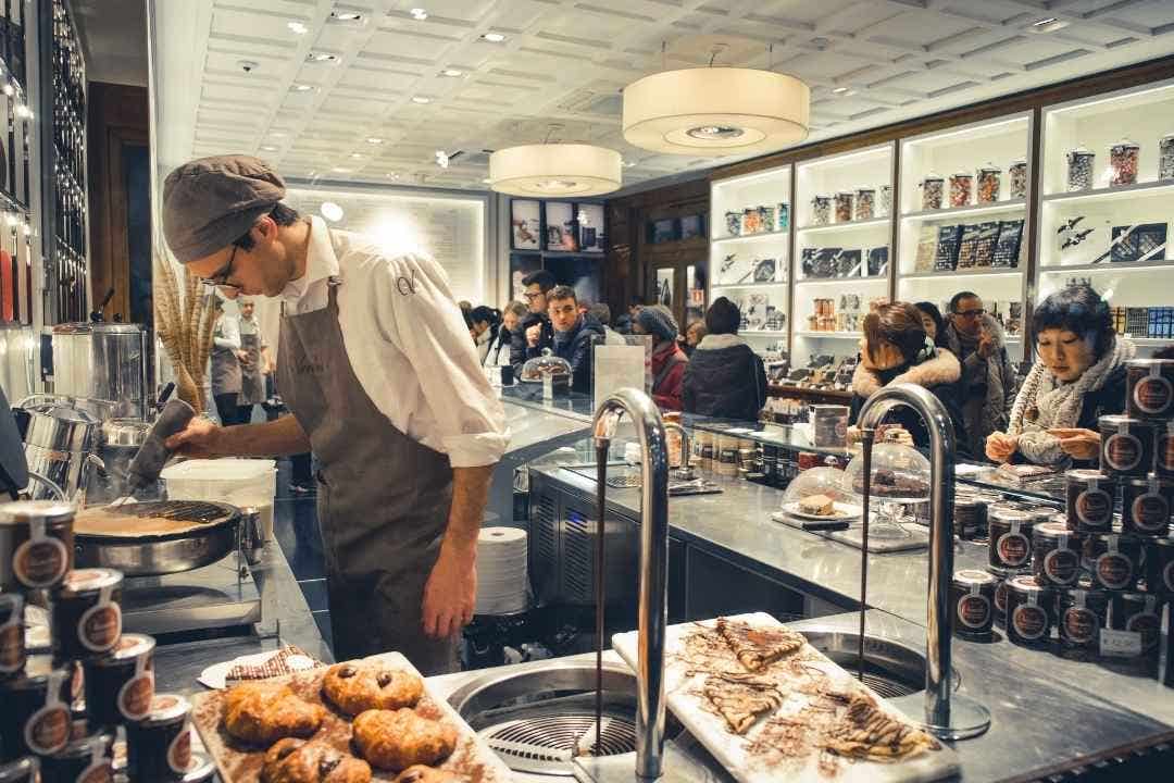 Pastry chef preparing desserts in a busy bakery with customers in the background