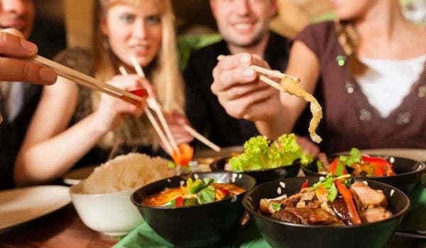 Friends enjoying an authentic Asian dining experience with chopsticks and shared dishes.