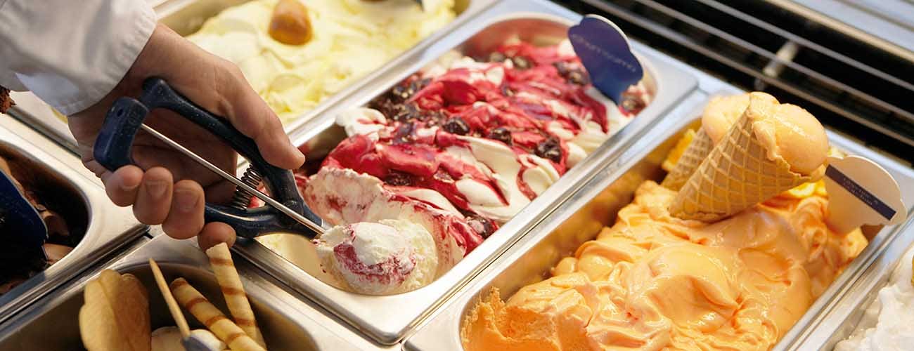 Close-up of a man scooping ice cream from tub in an ice cream parlor.