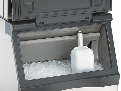 An Scotsman ice machine with it's door open, full of ice and a white ice scoop in it.