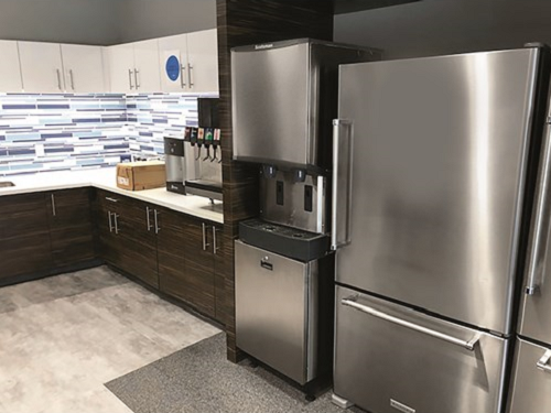 A Scotsman commercial water dispenser is pictured next to a reach-in refrigerator in a breakroom.