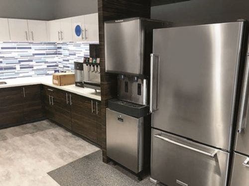 A Scotsman commercial water dispenser is pictured next to a reach-in refrigerator in a breakroom.