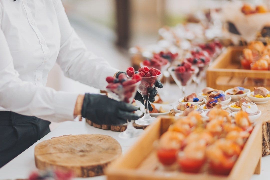 Caterer in gloves preparing dessert cups at a gourmet event buffet table.