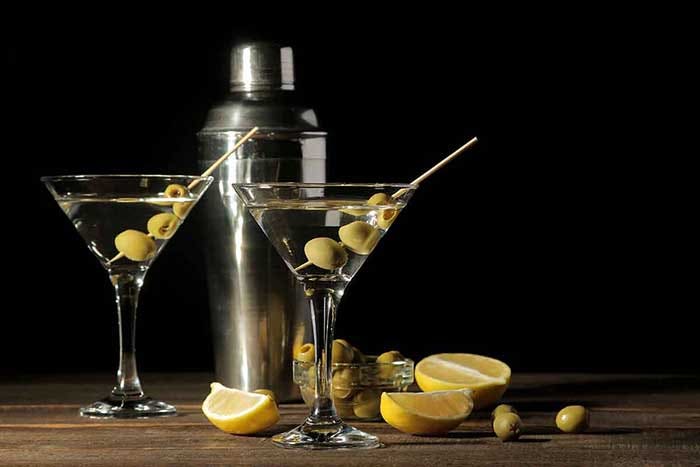 Martini in a glass wineglass with green olives on a skewer on a brown wooden table.