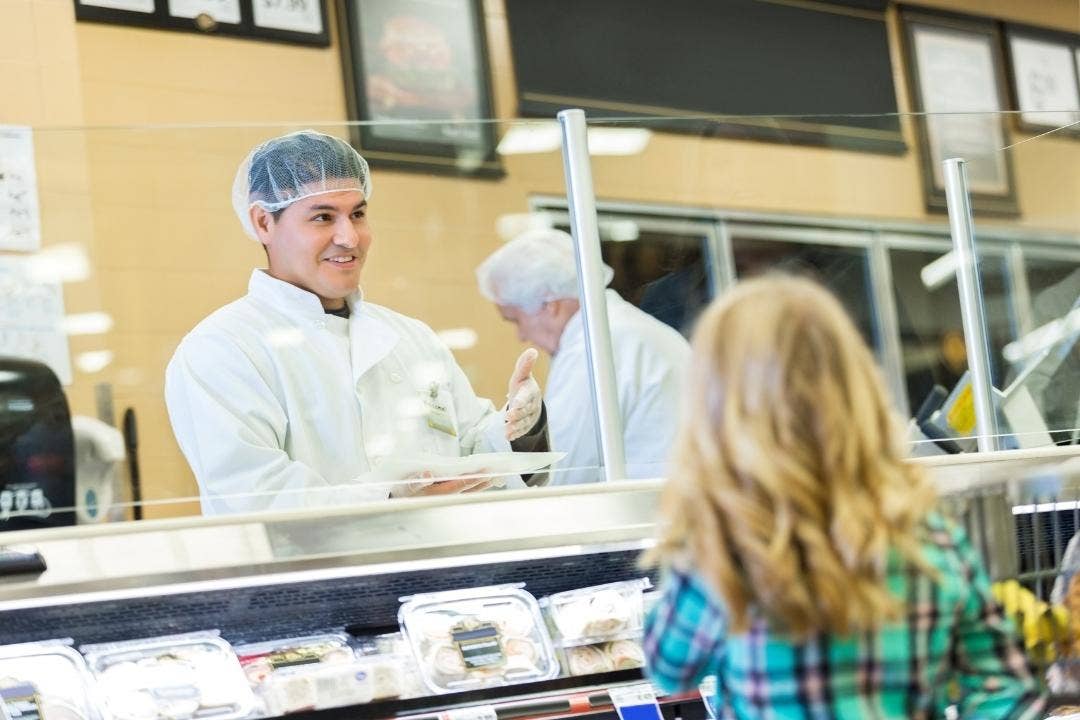 Smiling deli worker assisting customer at a grocery store meat counter